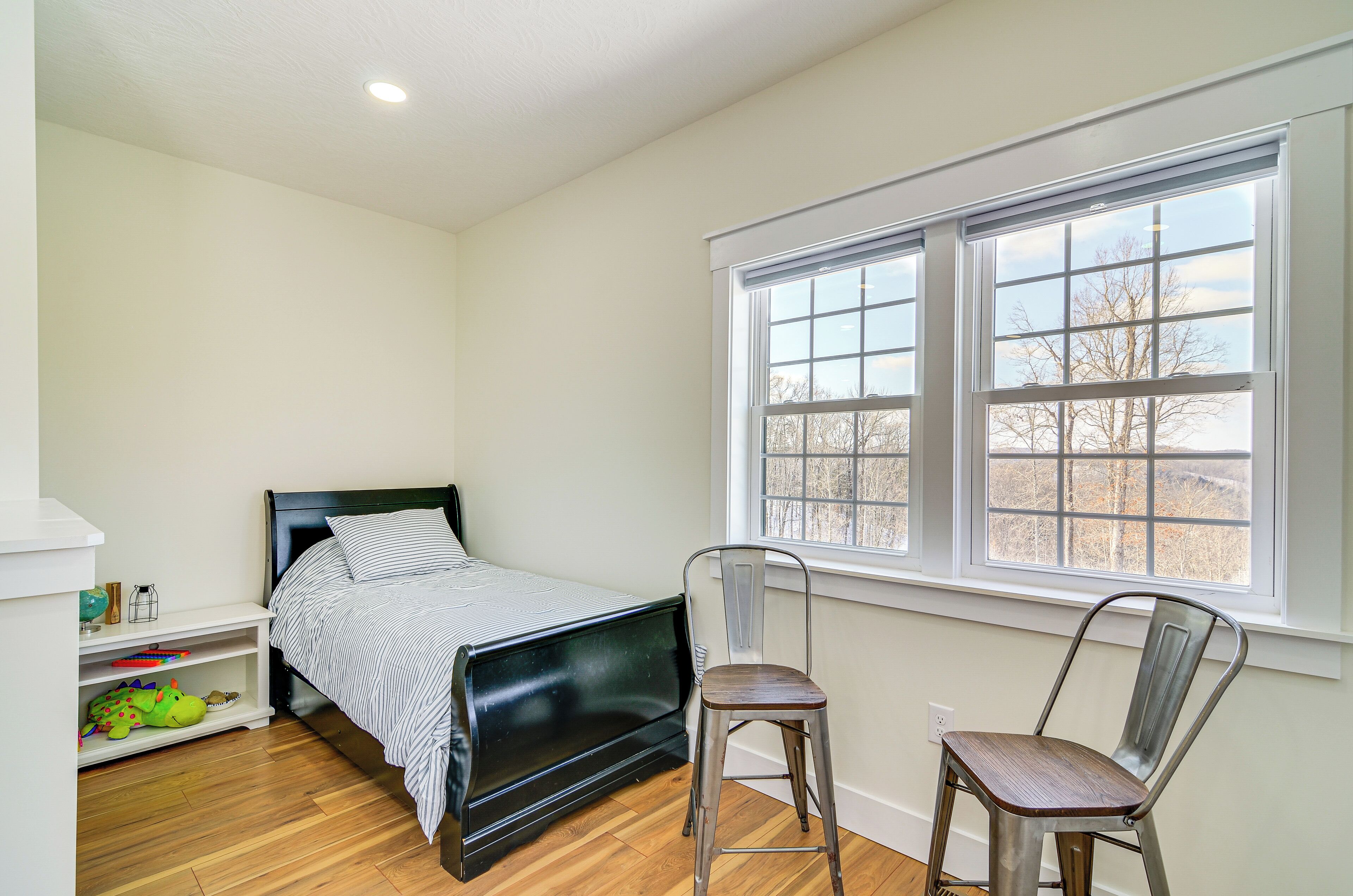 A bedroom with a bed, a chair, a window, and a shelf with toys.