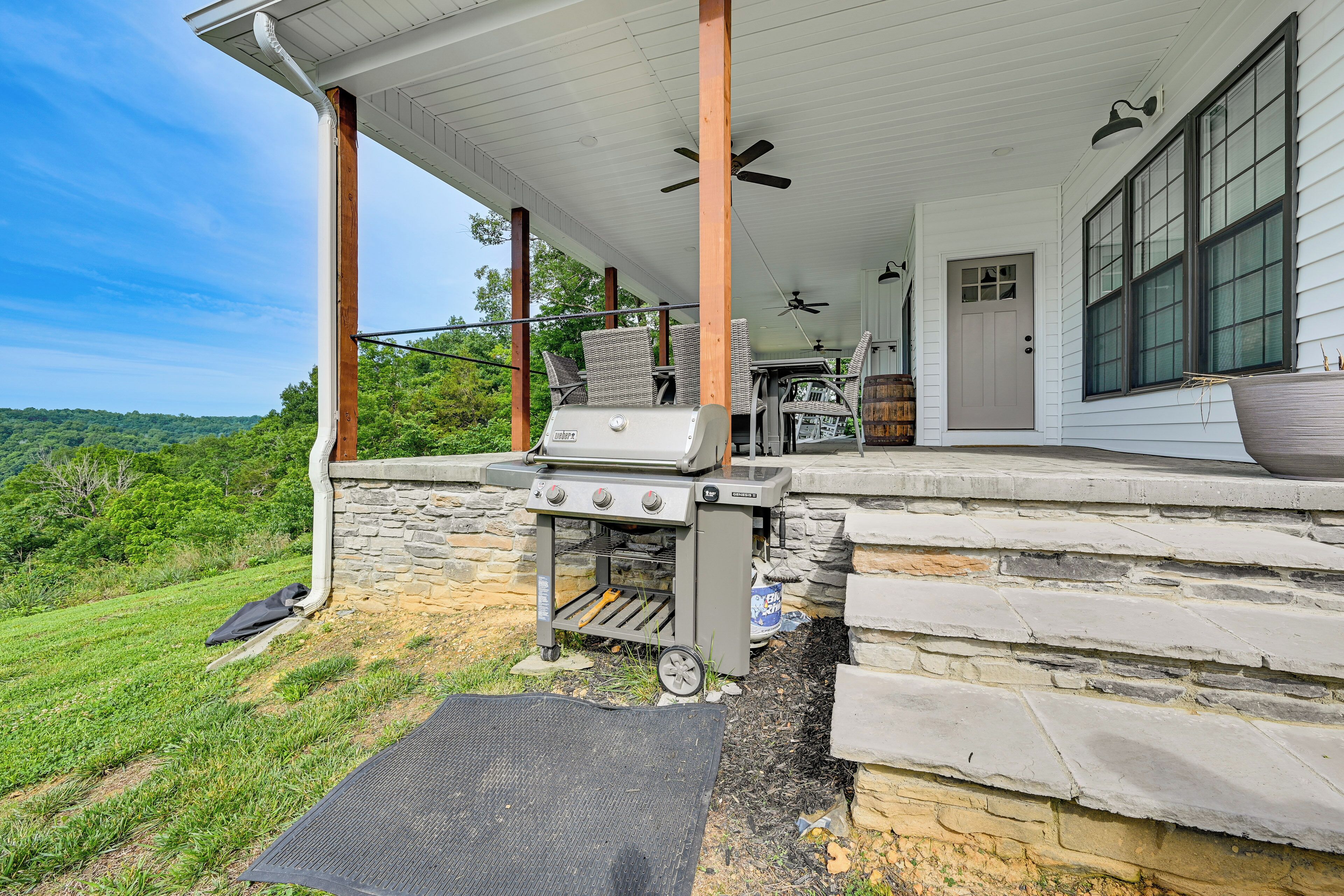 A covered porch with a grill, stone steps, and a door.