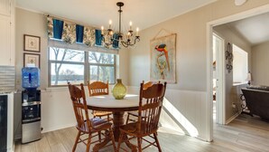 A dining area with a round table, wooden chairs, a chandelier, a water dispenser, and a window with curtains. - On-site Lake Access + Fire Pit: Bonham Home! (Bonham)