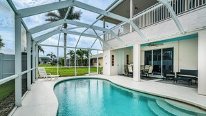 A swimming pool with a covered patio area, outdoor furniture, and a view of the surrounding neighborhood. - Hot Tub + Fire Pit: Spacious Cape Coral Oasis! (Cape Coral)