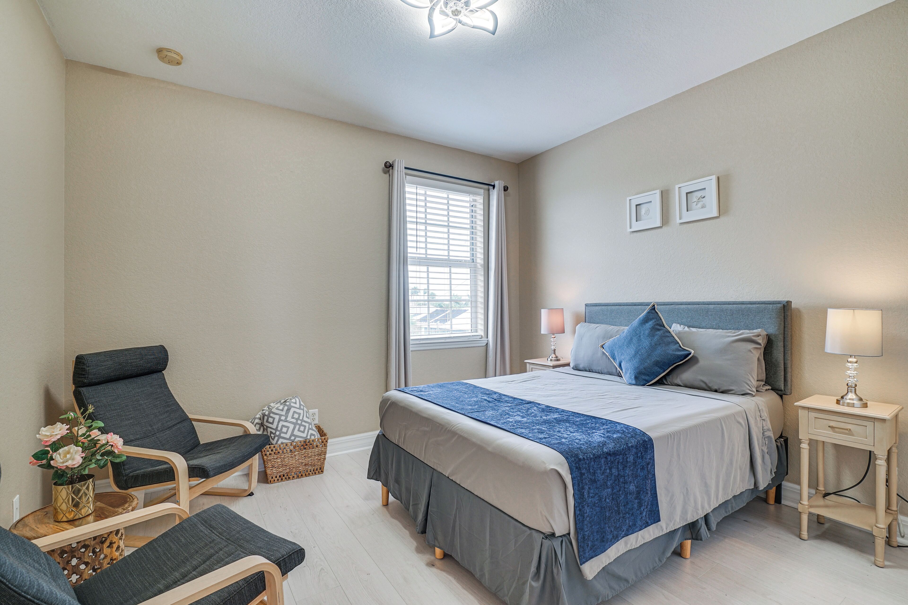 A bedroom with a bed, two bedside tables, a chair, a small table with a vase, and a window with curtains.