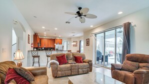 A spacious living room with a sofa, armchair, and coffee table, a kitchen area with wooden cabinets, and a ceiling fan. - Hot Tub + Fire Pit: Spacious Cape Coral Oasis! (Cape Coral)