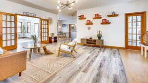Un vaste espace de vie doté d’un grand plancher en bois, d’un canapé, d’un fauteuil et d’une table à manger. Des étagères ornées d’objets décoratifs sont fixées aux murs, et une pancarte indique : « Laissez vos espoirs s’apaiser ».
