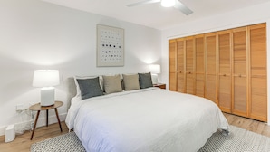Ein Schlafzimmer mit einem Bett, Nachttischlampen, einem Deckenventilator, einem hölzernen Kleiderschrank und einem an der Wand befestigten Lichtschalter.