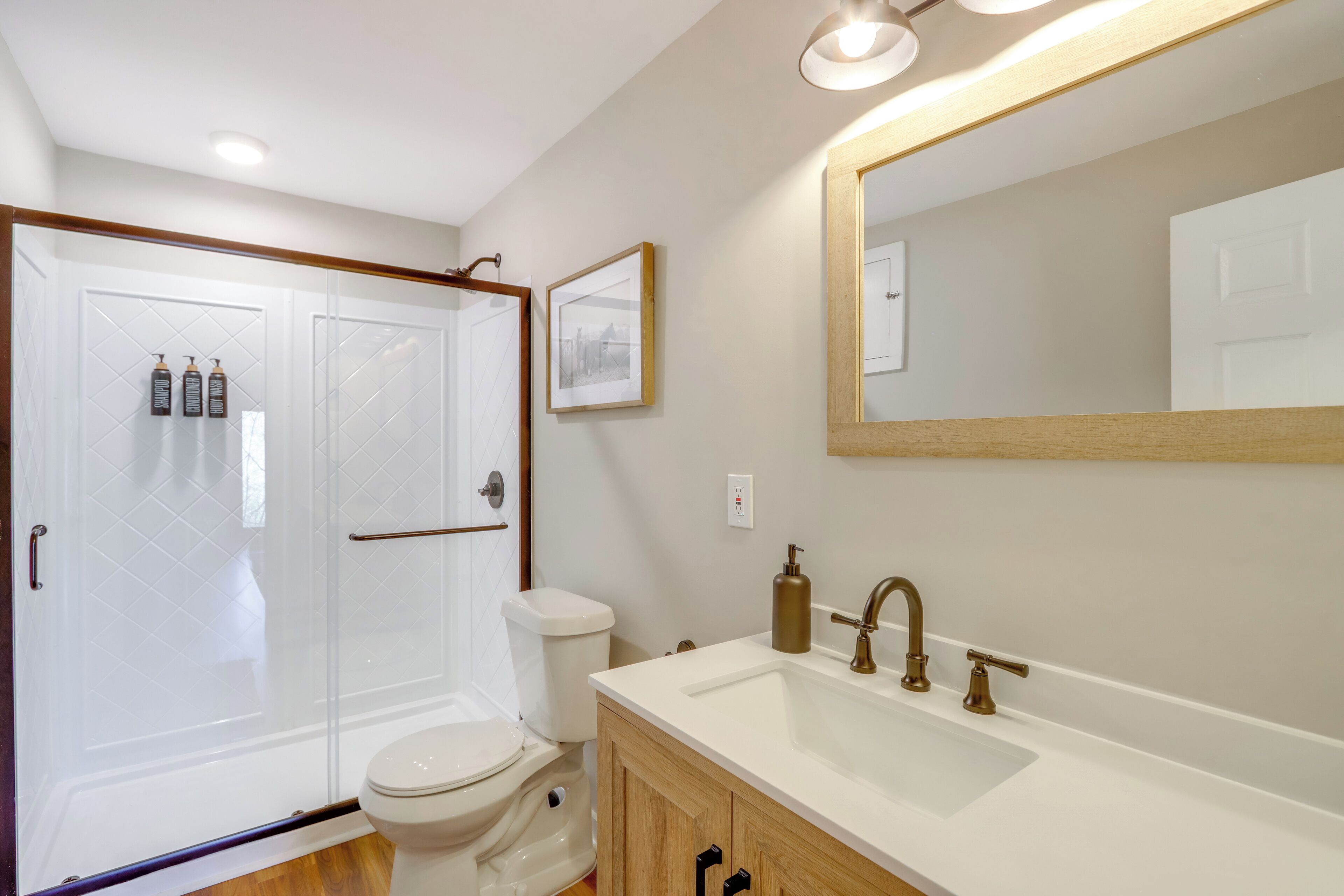 Ein Badezimmer mit Glasdusche, Toilette, Waschbecken mit Spiegel und einem gerahmten Bild an der Wand.