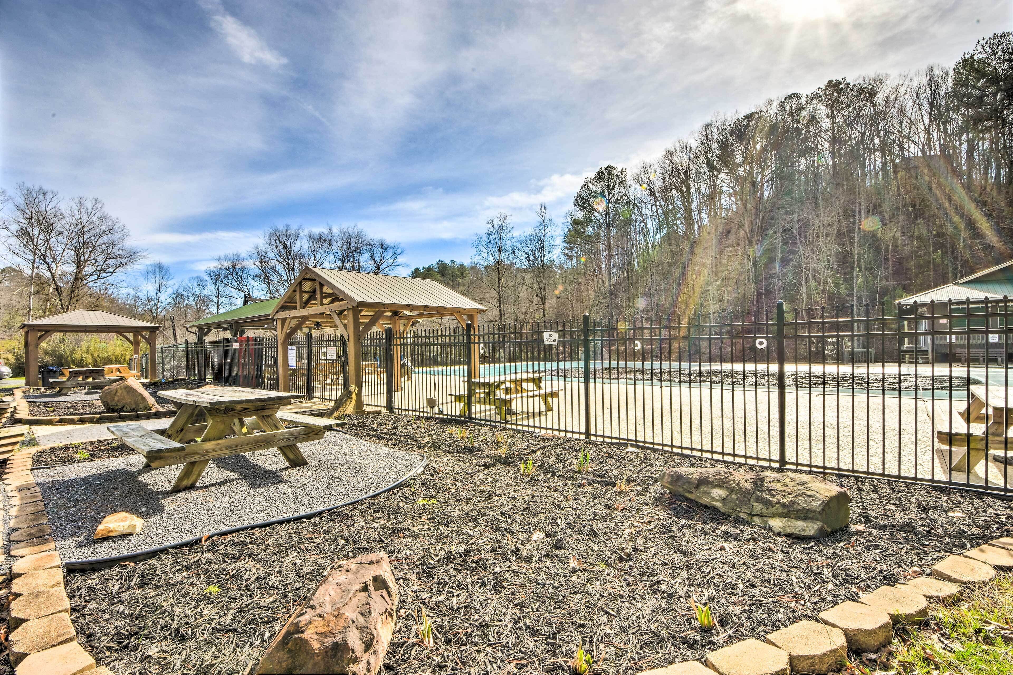 A fenced outdoor area with picnic tables, a small shelter, and a pool.