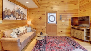 A wooden cabin interior with a sofa, a small round table, a TV, and a patterned rug. - Peaceful Ellijay Cabin: Pool Access & Resort Perks (Ellijay)