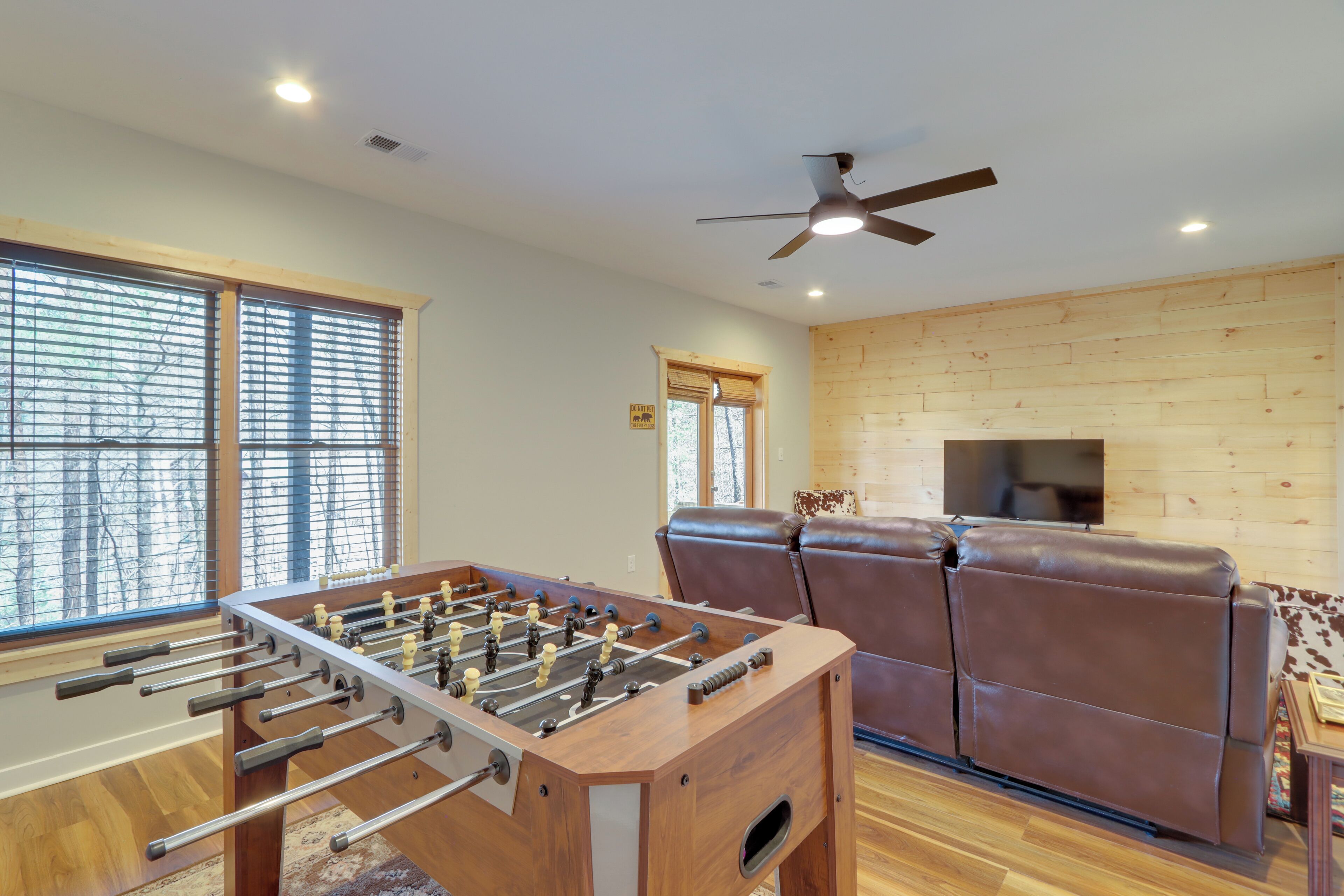 A room with a foosball table, leather recliners, a ceiling fan, and wooden walls.