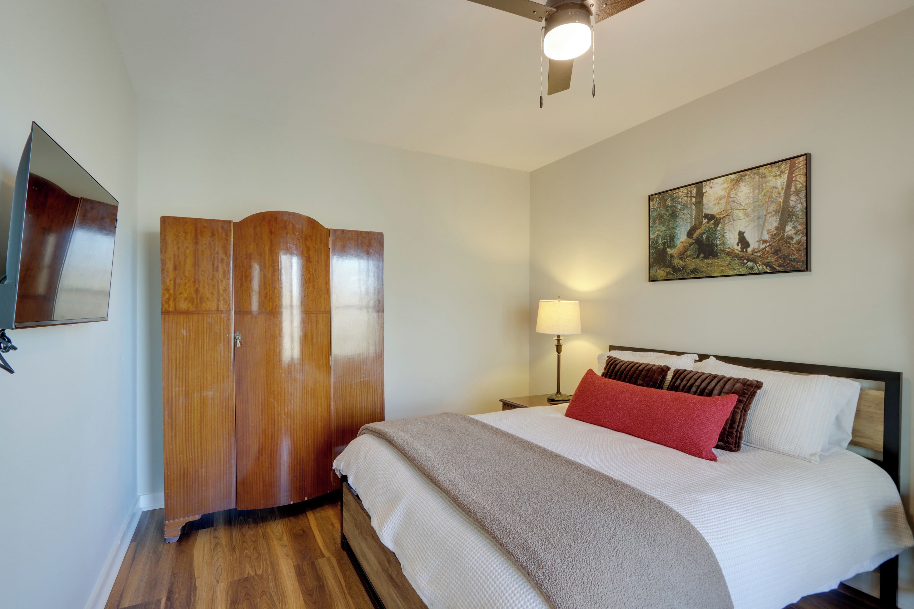 Une chambre à coucher avec un lit, une armoire, un tableau au mur et un ventilateur de plafond.