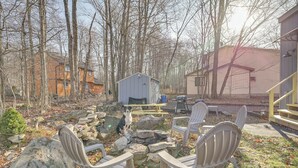 A rustic outdoor area with Adirondack chairs, a stone fire pit, and a small shed. - Fire Pit, Pool & Beach Access: Tobyhanna Home! (Tobyhanna)