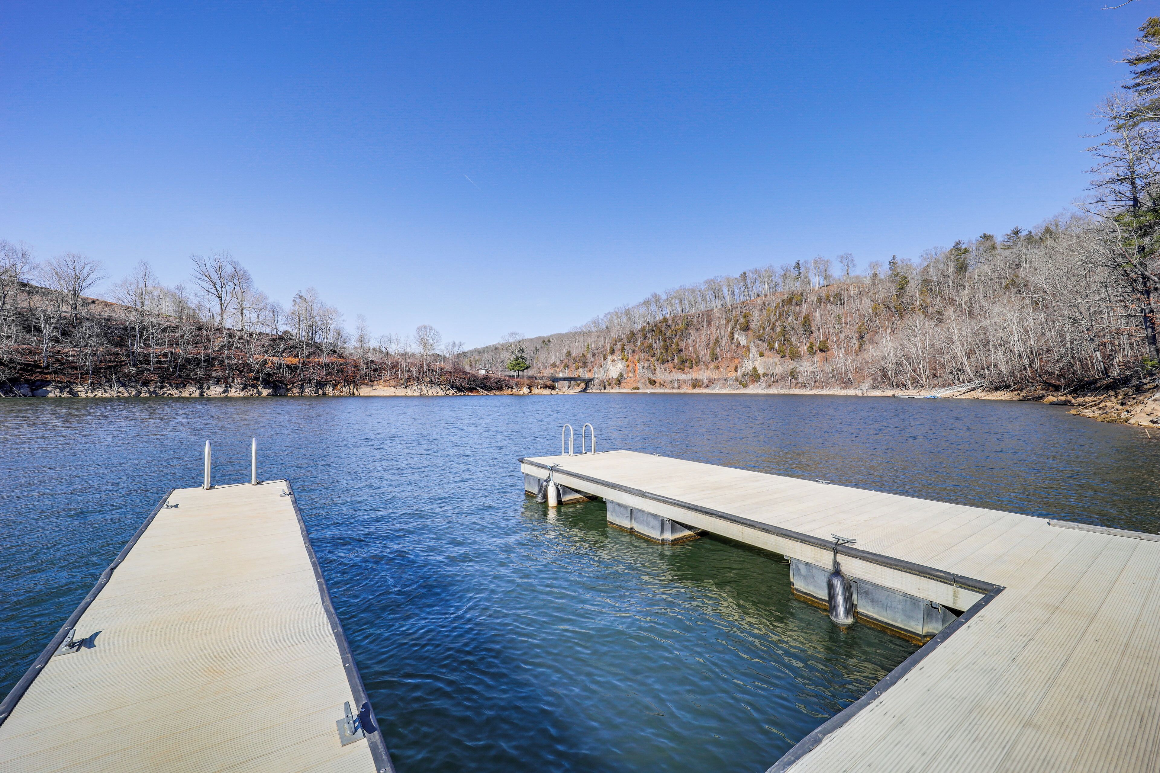 A wooden dock extending into a calm river, surrounded by trees and a clear sky.