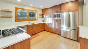 Una cocina moderna con armarios de madera, electrodomésticos de acero inoxidable y una ventana con vista a árboles.