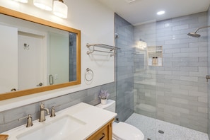 Een moderne badkamer met een wit wastafelmeubel, twee kraanwerkjes, een grote spiegel, een douchecabine van glas en een toilet.