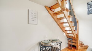 Un coin repas agrémenté d’un escalier en bois, d’une citation inspirante encadrée au mur et d’une petite table mise avec des assiettes et des verres.