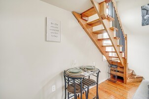 Un comedor con una escalera de madera, una cita inspiradora enmarcada en la pared y una pequeña mesa dispuesta con platos y vasos.