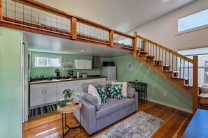 A spacious living area with a grey sofa, wooden staircase, and a kitchen in the background. - Pacheco/martinez Studio: 22 Mi to Dtwn Oakland! (Martinez)