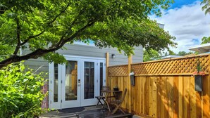 Une terrasse en bois avec une table et des chaises, une clôture en bois et une maison avec une porte et des fenêtres blanches.