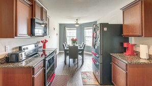 Una cocina con armarios de madera, encimera de granito, una mesa de comedor con sillas, un refrigerador y un microondas.