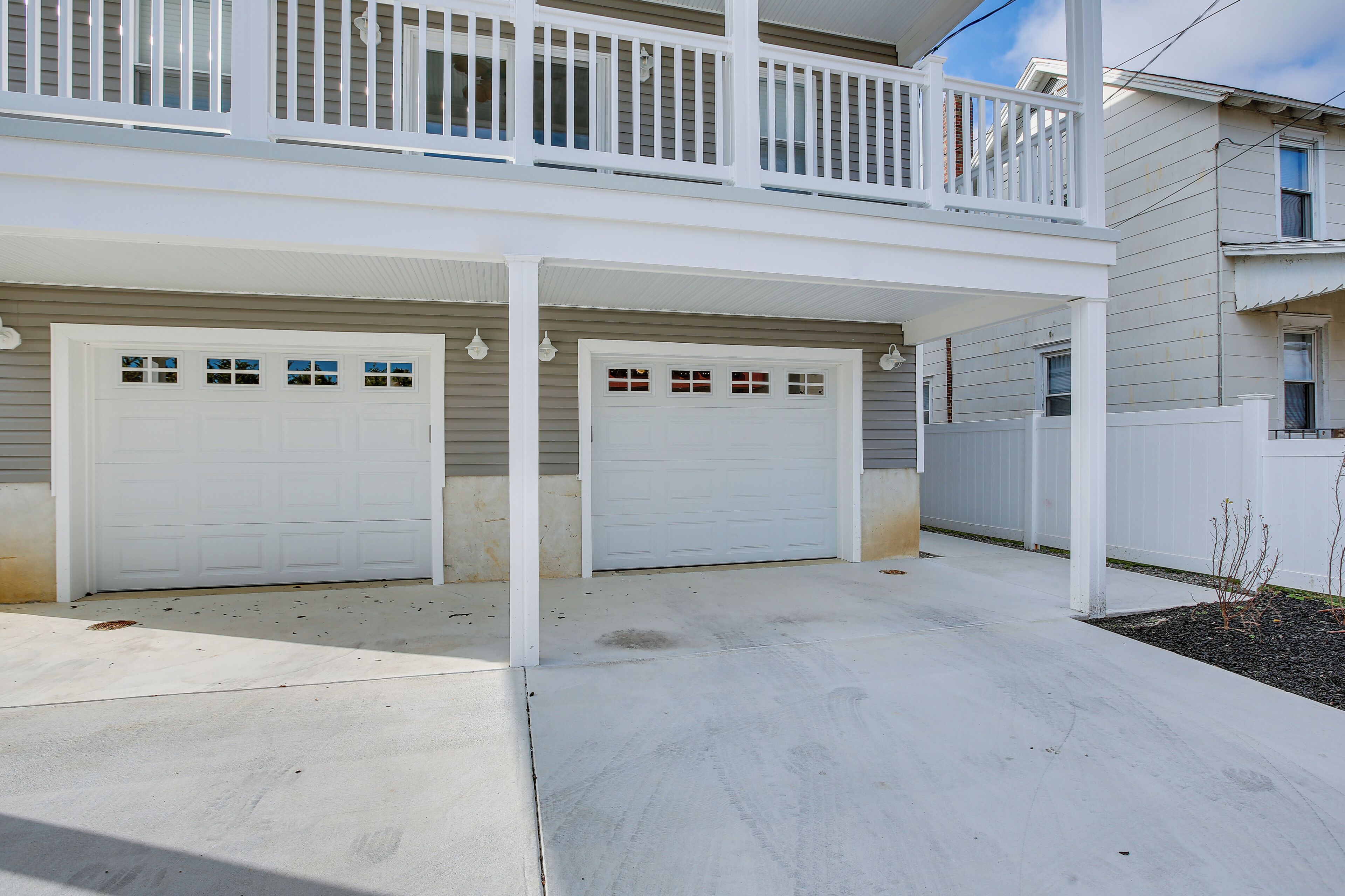 A two-story house with a covered front porch, two garage doors, and a small garden area.