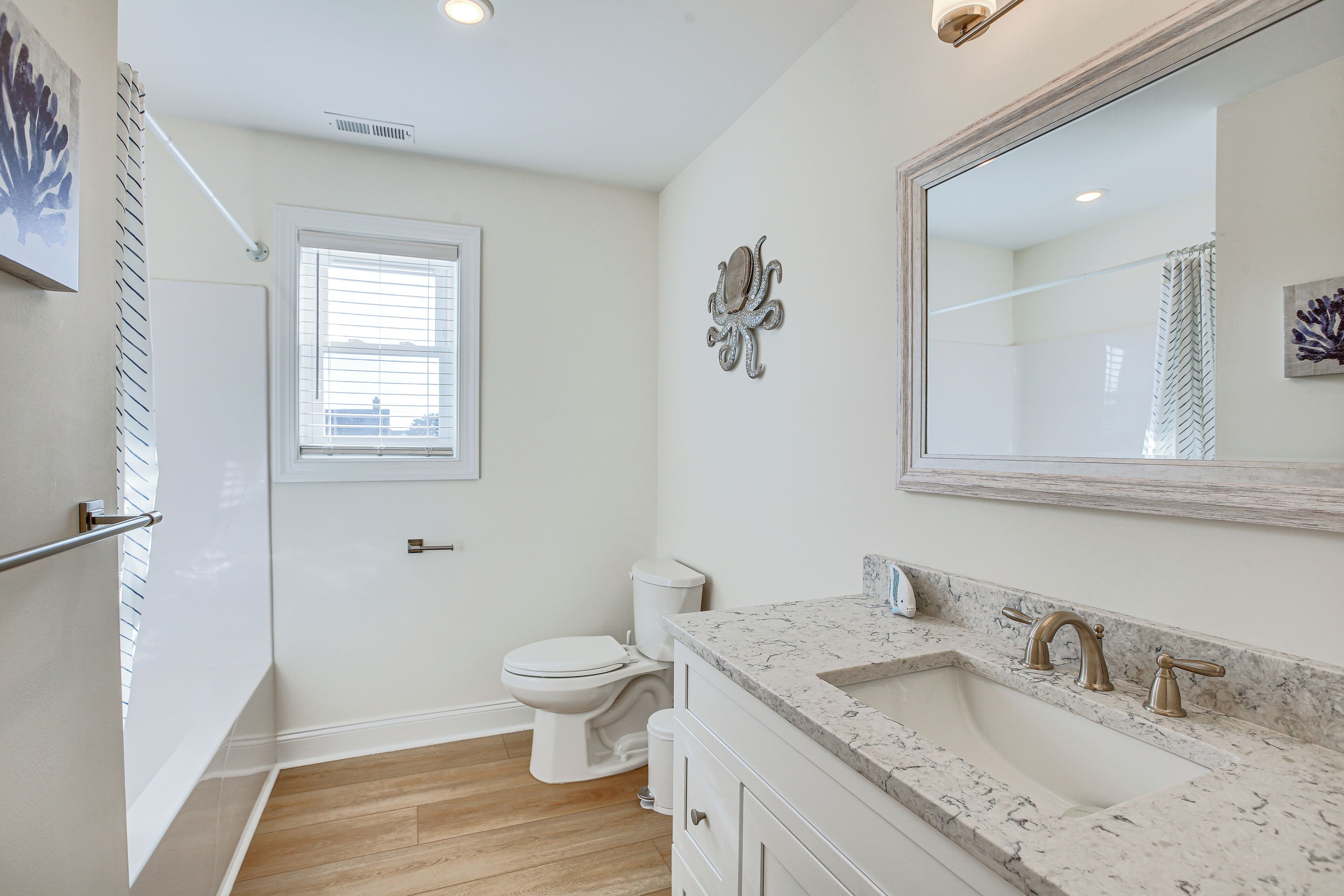 A bathroom with a white toilet, a sink with a marble countertop, and a large mirror.
