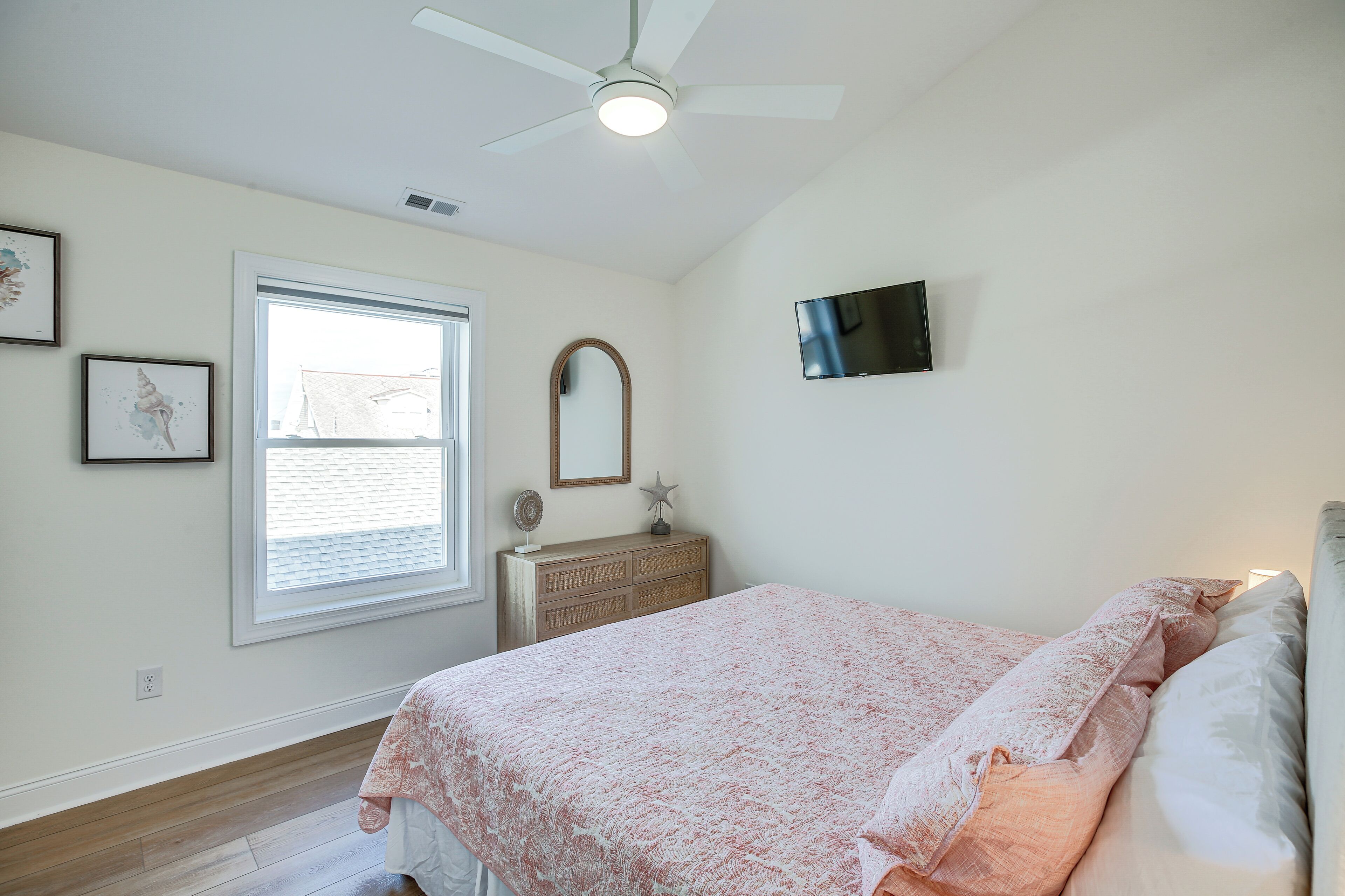 Une chambre à coucher comprenant un lit, une commode, un miroir, un ventilateur de plafond et un téléviseur.