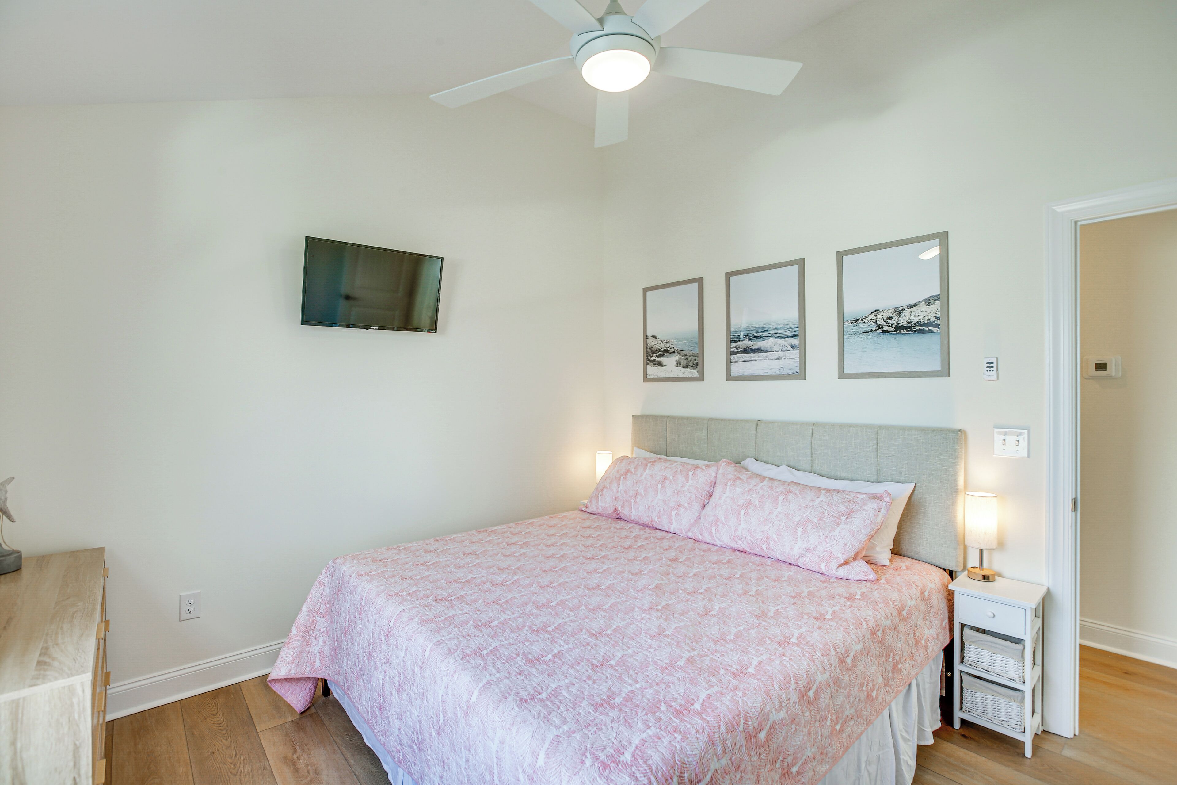 A bedroom with a bed, a ceiling fan, a nightstand, and wall-mounted artwork.