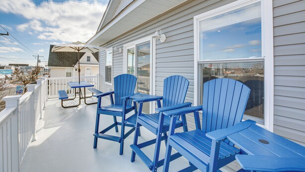 Een overdekte veranda met blauwe Adirondack-stoelen en een picknicktafel.