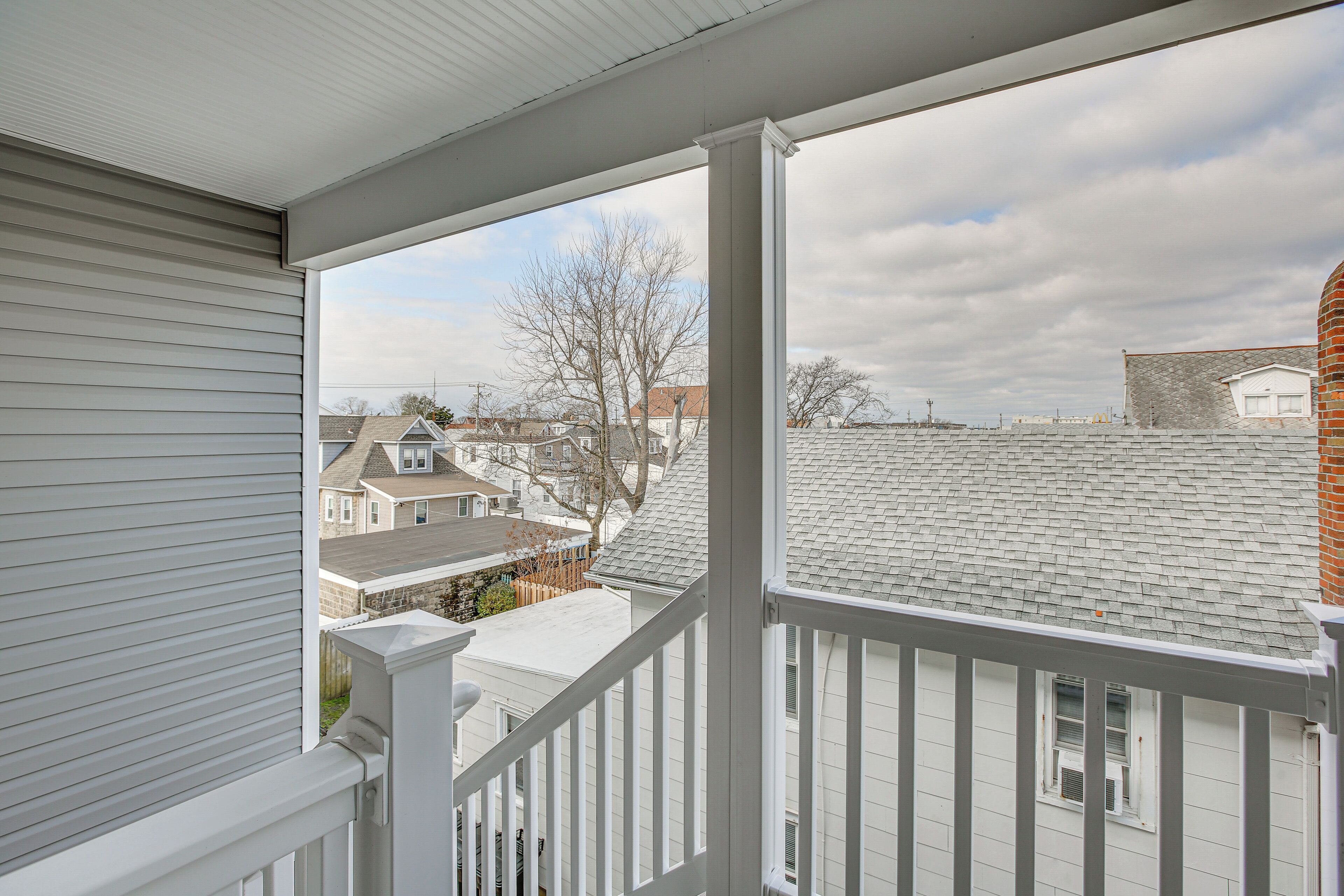 A balcony with a view of neighboring houses and a cloudy sky.