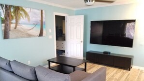 Un salon avec un canapé gris, une table basse, un téléviseur à écran plat posé sur un meuble noir et un tableau représentant une scène de plage.