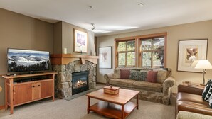 A cozy living room with a stone fireplace, a flat-screen TV, a wooden coffee table, and a comfortable sofa. - 1202 - Two Bedroom Standard Eagle Springs West 2 Condo by RedAwning (Solitude)