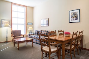 Cozy living room with a dining table, sofa, and armchair, surrounded by framed artwork and a large window.