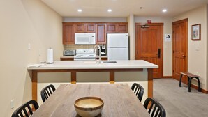 A kitchen with wooden cabinets, a white microwave, a white refrigerator, and a wooden dining table with chairs. - 3506 - One Bedroom + Den Standard Powderhorn Lodge 1 Condo by RedAwning (Salt Lake City)