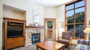 A living room with a fireplace, a television, a coffee table, a patterned armchair, and a sofa. - 3506 - One Bedroom + Den Standard Powderhorn Lodge 1 Condo by RedAwning (Salt Lake City)