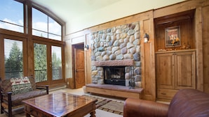 A spacious living room with a stone fireplace, wooden furniture, and large windows.
