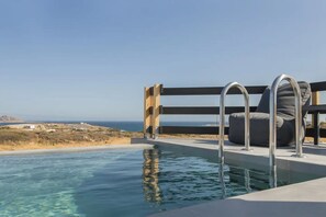 A pool with a wooden deck and a chair, overlooking a coastal landscape. - Maisonette whith amazing sea view. (Paros)