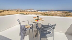 Ein Balkon mit zwei Stühlen, einem Tisch mit Flasche und Gläsern und einem schönen Blick auf den Strand und weiße Gebäude.