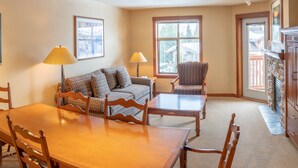 A cozy living room with a wooden dining table, two patterned sofas, a striped armchair, and a fireplace.