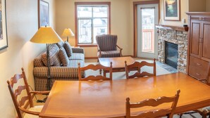 A dining area with a wooden table and chairs, a patterned sofa, and a stone fireplace.