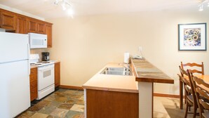A kitchen with wooden cabinets, a white refrigerator, a microwave, a stove, a sink, and a dining table with chairs.