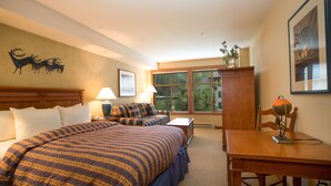 Une chambre d’hôtel avec un grand lit, un bureau et une chaise. Il y a une fenêtre donnant sur des arbres et une décoration murale représentant un cerf.