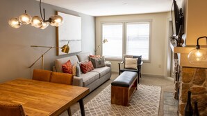 A modern living room with a wooden dining table, a gray sofa with patterned cushions, a bench, and a stone fireplace. - 2204 - Two Bedroom Deluxe Eagle Springs East 2 Condo by RedAwning (Solitude)