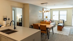 A modern kitchen with a central island, a dining area with a wooden table and chairs, and a living area with a sofa and a bench. - 2204 - Two Bedroom Deluxe Eagle Springs East 2 Condo by RedAwning (Solitude)