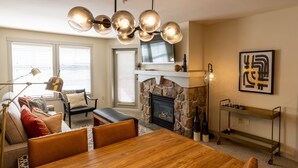 A modern living room with a wooden dining table, leather chairs, a stone fireplace, a mounted TV, and a contemporary art piece. - 2204 - Two Bedroom Deluxe Eagle Springs East 2 Condo by RedAwning (Solitude)