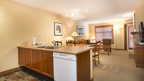 A compact kitchen with a dishwasher, a dining area with a table and chairs, and a small seating area with a lamp. - 3212 - One Bedroom Standard Powderhorn Lodge 1 Condo by RedAwning (Salt Lake City)