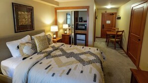 A hotel room with a bed, bedside lamps, a desk, a chair, a refrigerator, and a door. - 1205b - Double Queen Standard Eagle Springs West 1 Bedroom Hotel Room by RedAwning (Solitude)