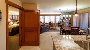 A spacious living area with a kitchen, a dining table, and a large wooden door leading to a bedroom. - 2215 - Two Bedroom Deluxe Eagle Springs East 2 Condo by RedAwning (Solitude)