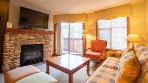 A living room with a stone fireplace, a flat-screen TV mounted above it, a wooden coffee table, a plaid sofa, and two armchairs. - 3309A - One Bedroom Standard Powderhorn Lodge 1 Condo by RedAwning (Salt Lake City)