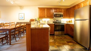 A kitchen with wooden cabinets, a stainless steel refrigerator, a microwave, and a dining area with a table and chairs. - 3309A - One Bedroom Standard Powderhorn Lodge 1 Condo by RedAwning (Salt Lake City)