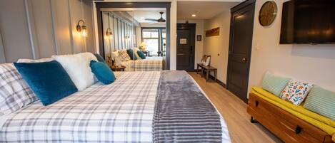 Un dormitorio con una cama grande, un banco de madera, un televisor y una puerta que da a otra habitación.