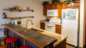 Una cocina con encimera de granito, armarios de madera, microondas, estufa y refrigerador.